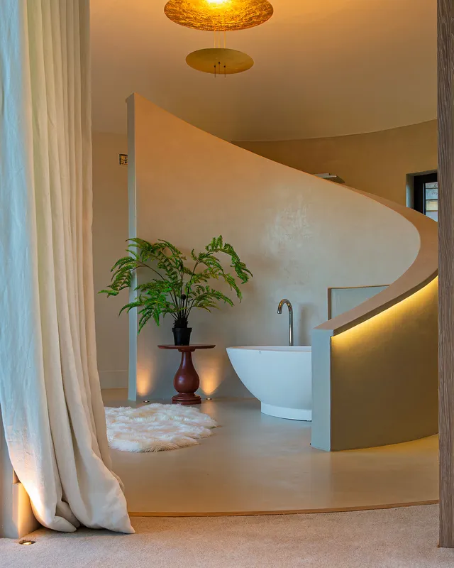 A striking decorative pendant, uplighting and a curved linear fiiting combine to light a modern curved bathroom