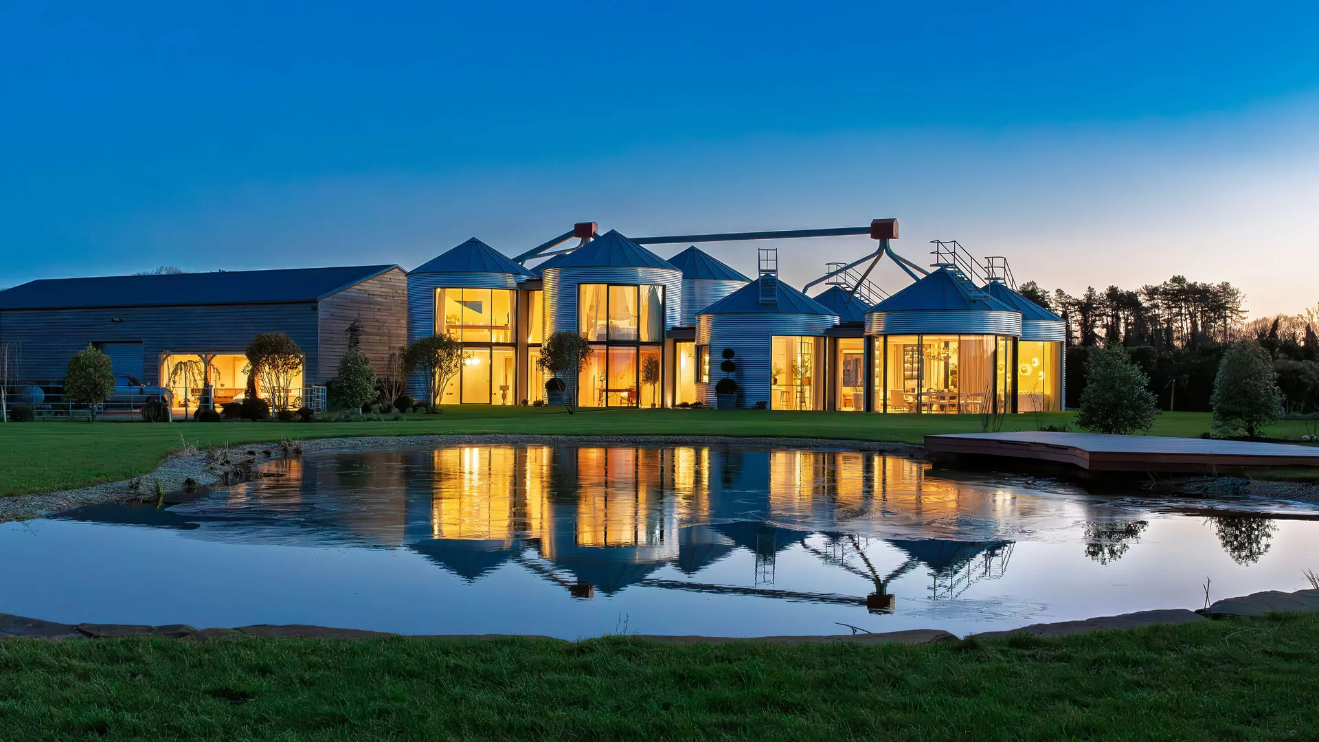 Evening shot of a luxury country house built around an array of agricultural silos