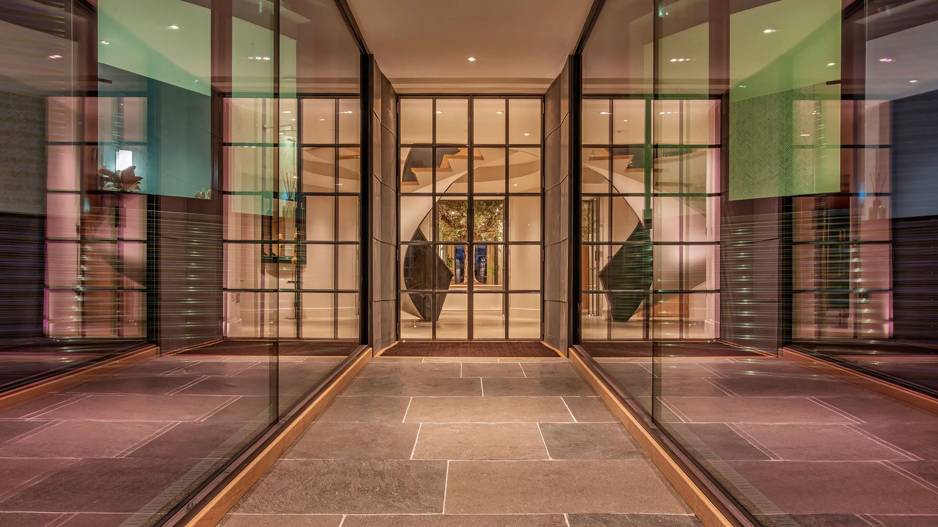Looking down a glazed link towards the uplit helical staircase and olive tree