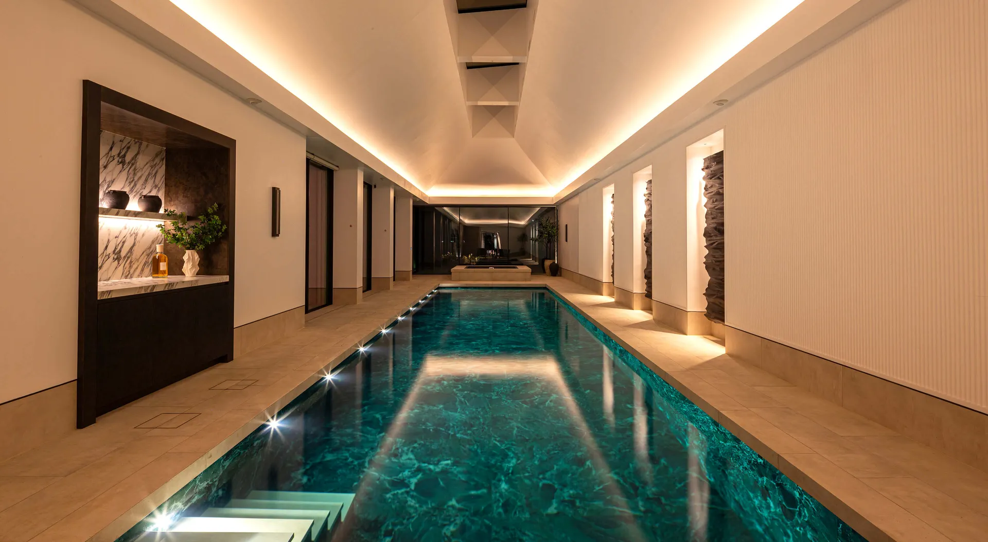 A beautifully tiled swimming pool with coffer lighting in a pitched ceiling