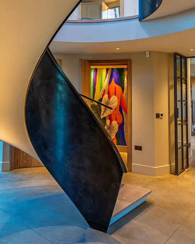 Uplit helical staircase in a modern house with a vibrant bright bathroom behind.